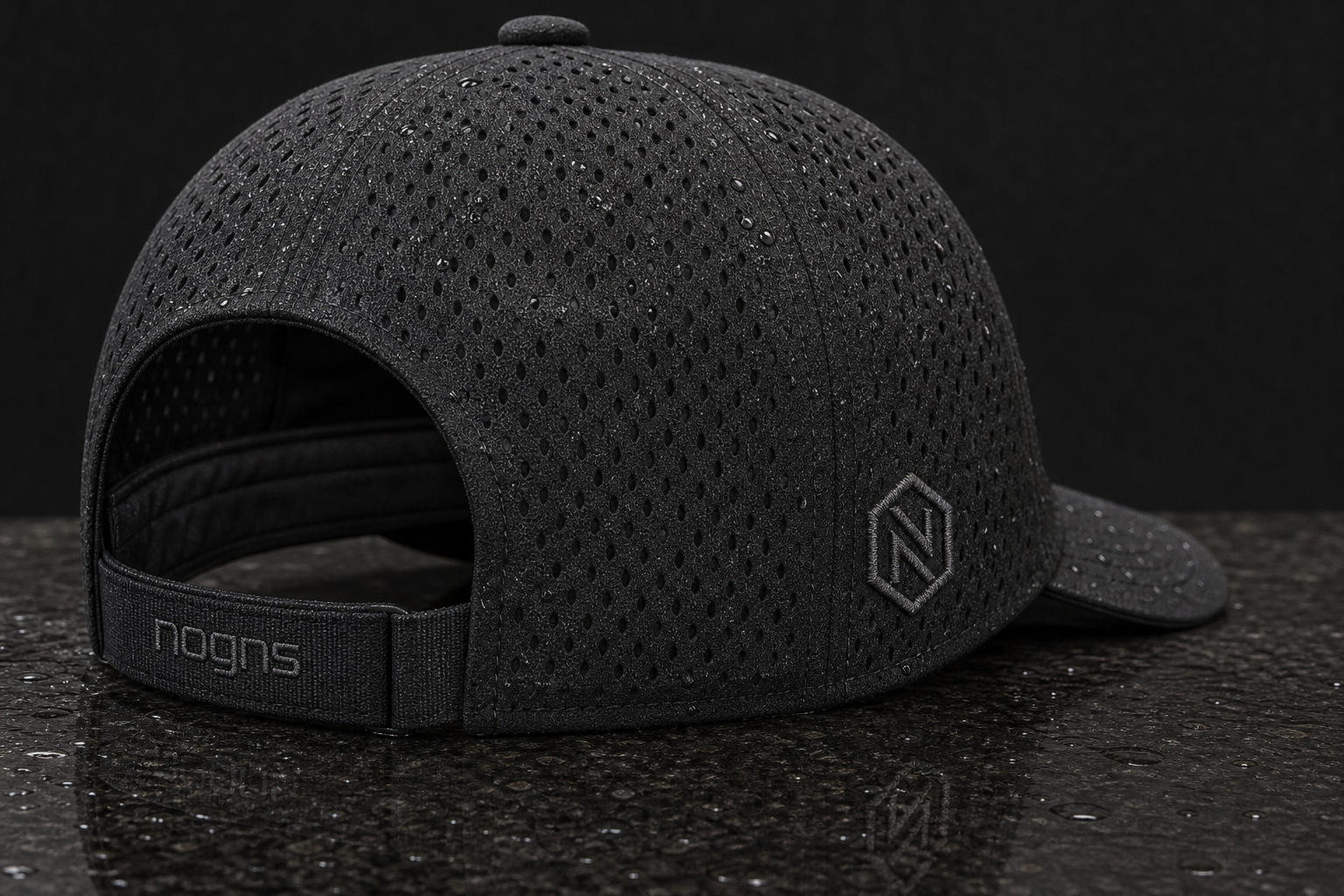 Macro rear view of a black NOGNS embroidered cap — perforated shell beading water, tonal hex N stitched into the side panel, and lowercase nogns embroidered on the rear closure strap.